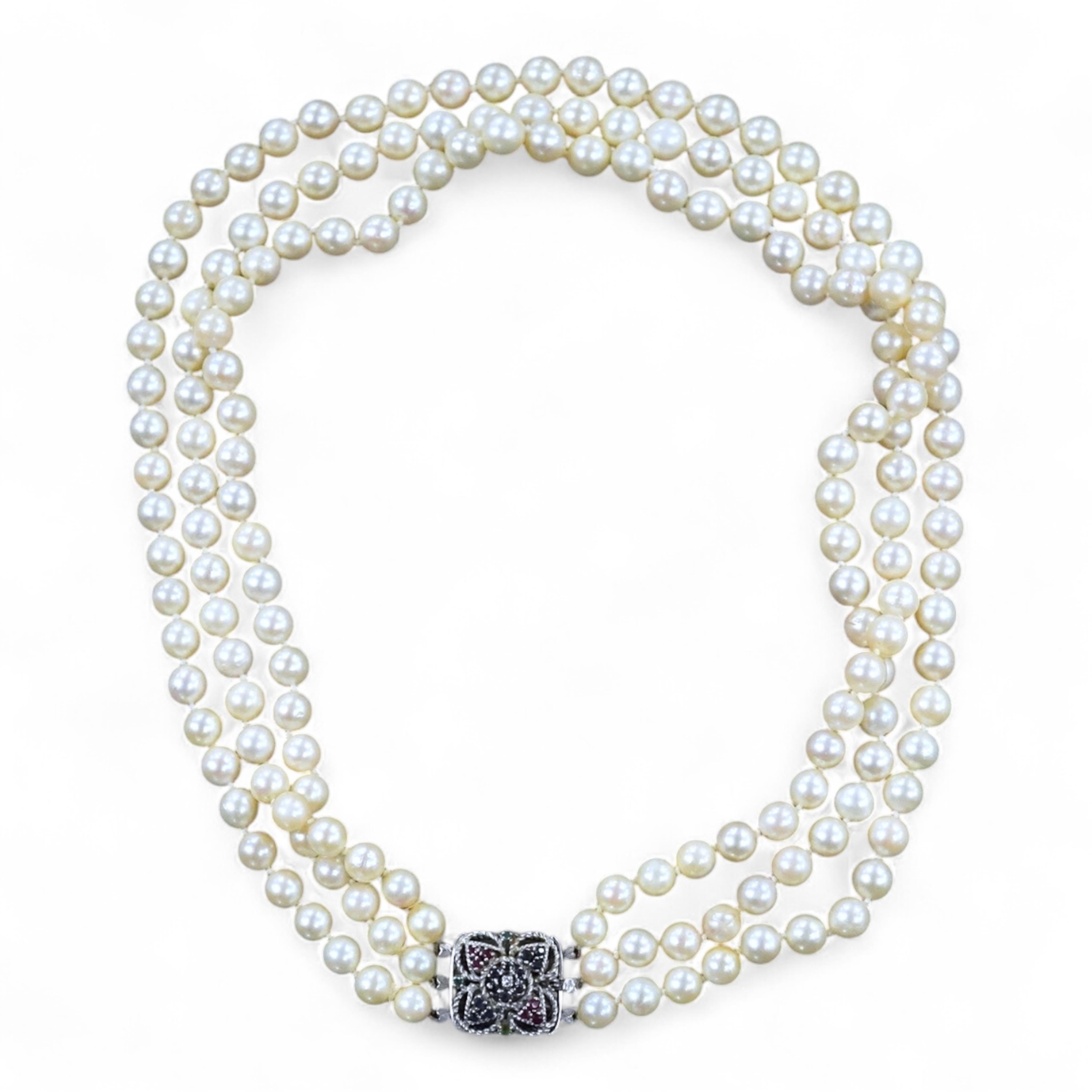 A triple strand cultured pearl necklace, with an Italian 18k white metal, ruby, sapphire and emerald set clasp, 46cm.
